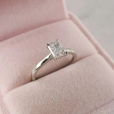 an engagement ring with a princess cut diamond in a pink velvet box on the floor