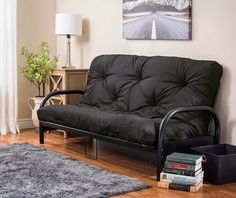 a black futon sofa sitting on top of a wooden floor next to a lamp