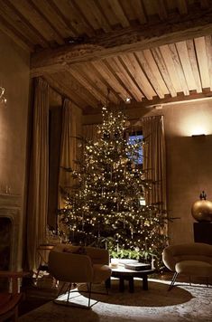 a living room with a lit christmas tree in the corner and two chairs around it