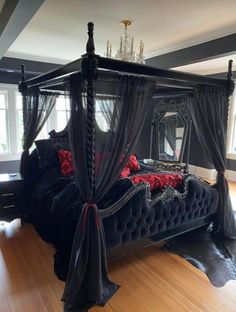 a black bed with red pillows on top of it and a chandelier hanging from the ceiling