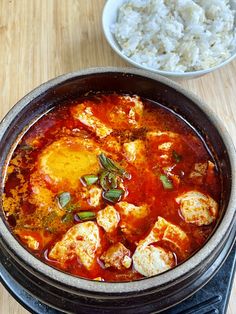 a bowl filled with food next to rice on top of a wooden table