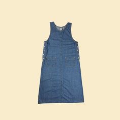 Vintage sleeveless denim maxi dress, manufactured ca. 1990s by Tape Measure. This A-line dress features two front pockets, metal side buttons, and is a size M.  - Time Period: c. 1990s  - Brand: Tape Measure  - Size: M  - Colors: Medium-wash denim blue  - Materials: 100% cotton  - Made in: Guatemala  - Condition: In fair to good, vintage condition. Has some markings on the front, shown in photos with hand. Please see the close-up photos and let us know if any additional details would be helpful. Fitted Sleeveless Buttoned Denim Jumpsuit, Spring Sleeveless Denim Jumpsuit With Button Closure, Fitted Sleeveless Denim Jumpsuit With Buttons, Sleeveless Dark Wash Dress With Buttons, Sleeveless Denim Maxi Dress Fitted, Sleeveless Pinafore Dress With Buttons For Summer, Vintage Blue Sleeveless Denim Dress, Sleeveless Denim Jumpsuit With Button Closure For Summer, Sleeveless Denim Maxi Dress