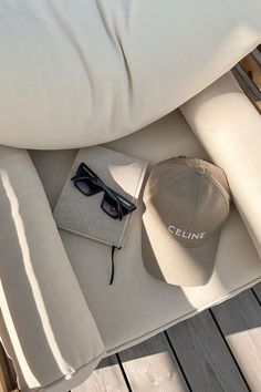 a hat, sunglasses and book sitting on top of a white couch next to pillows