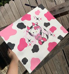 someone is holding up a hello kitty painting on a wooden fence with pink and black hearts