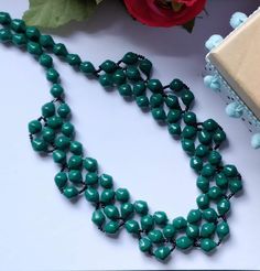 a green necklace is sitting on a table next to a box and rosebud