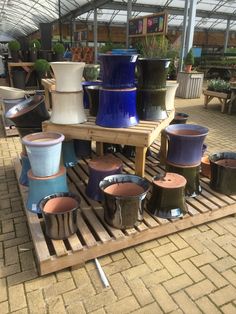 many different colored pots are stacked on a wooden pallet in a garden center area