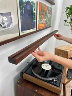 a person is touching a record player with their hand on the turntable and some pictures are hanging above them