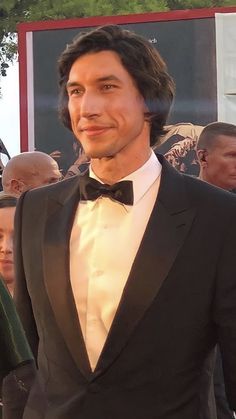 a man in a tuxedo and bow tie standing on a red carpet at an event