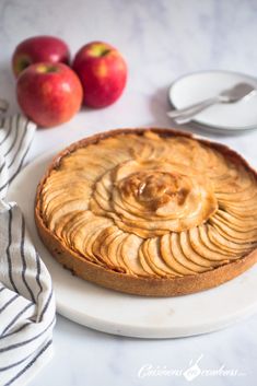 an apple pie on a white plate with apples in the background