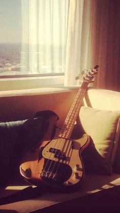 a bass guitar sitting on top of a couch next to a window