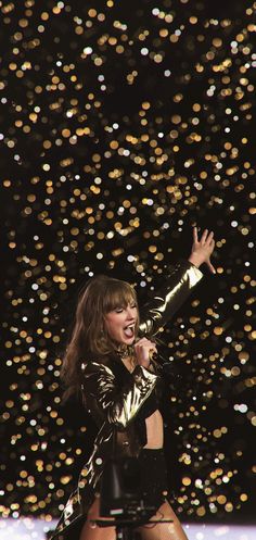 the woman is singing on stage with her hands in the air and sparkling lights behind her