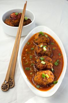 two bowls filled with food next to chopsticks on a white tablecloth covered table