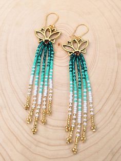 the earrings are made with beads and gold - plated metal, on top of a piece of wood