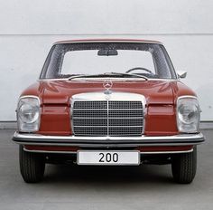 an old red mercedes is parked in front of a white wall