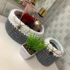 two crocheted baskets with plants in them on a white countertop next to a mirror