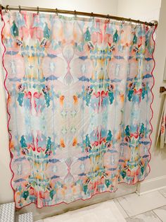 a colorful shower curtain hanging on the side of a bath tub in front of a tiled floor