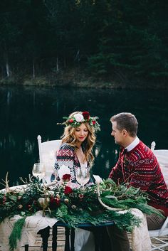 a man and woman sitting at a table with christmas decorations on it in front of a lake