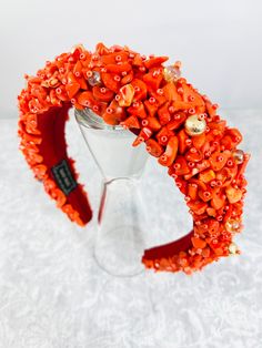 an orange headband with buttons and beads on it sitting on top of a glass stand