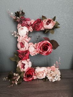 the letter e is made up of flowers and leaves on top of a wooden table