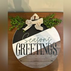 a wooden sign that says seasons greetings with greenery around it and a bow on top