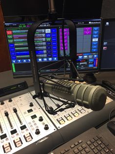 a microphone sits in front of two computer monitors and sound mixing equipment on a desk