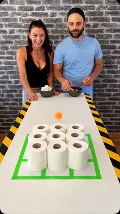 a man and woman standing behind a table with rolls of toilet paper on top of it