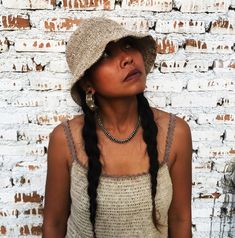 a woman wearing a hat standing in front of a brick wall with her eyes closed