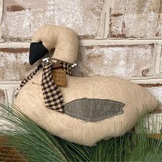 a stuffed duck sitting on top of grass next to a brick wall with a tag in it's ear