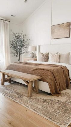 a bedroom with a large bed, wooden bench and rugs on the hardwood floor