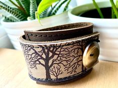 "I've made this wrapping cuff out of either soft brown or black base leather and an olive taupe leather with a hand printed with an image using indelible ink. Machine stitched, it has an attached elastic that hooks over a button, so this cuff will adjust to fit most wrist sizes 5.75\" to 7\" in circumference or select a CUSTOM SIZE in the drop down menu. At the narrowest, the width of the cuff is 1.25\" and at the widest it's 2\". Only premium quality leather and supplies are used to handcraft e Brown Everyday Cuff Bracelet, Everyday Brown Cuff Bracelet, Adjustable Brown Cuff Bracelet, Leather Strap Cuff Bracelet Gift, Adjustable Cuff Leather Bracelet, Cuff Bracelets With Leather Strap As Gift, Cuff Bracelet With Leather Strap For Gift, Unique Brown Cuff Bracelet, Handmade Brown Cuff Bracelet