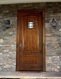 a wooden door sitting on the side of a stone wall next to two light fixtures