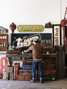 a man working in a shop with lots of old suitcases and signs on the wall