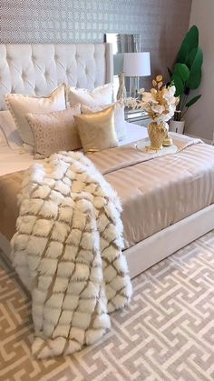 a white bed with pillows and blankets on top of it next to a vase filled with flowers