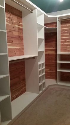 an empty walk in closet with white shelves and wood paneling on the wall behind it