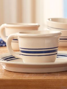 two white cups and saucers on a wooden table with blue striped dishes in the background