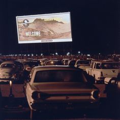 cars are parked in a parking lot with a welcome sign on the wall behind them