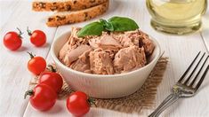 a white bowl filled with tuna and cherry tomatoes next to sliced bread on a table