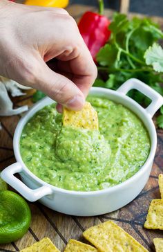 a person dipping guacamole into a bowl with tortilla chips