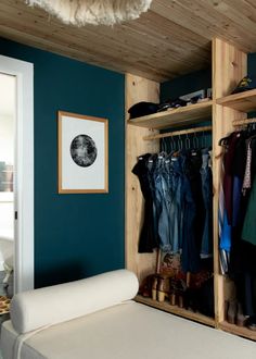 a bedroom with blue walls and clothes hanging on wooden shelves next to a white couch