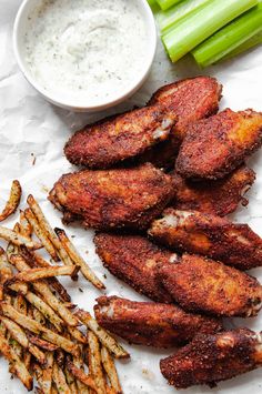 chicken wings, french fries and dip on a white paper with celery sticks