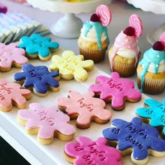 some decorated cookies are on a table with cupcakes and other desserts in the background