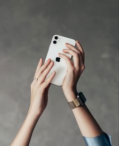 two hands holding up an iphone in front of a gray background, with the screen partially covered by one hand