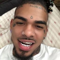 a man with piercings on his forehead and nose smiles at the camera while lying in bed