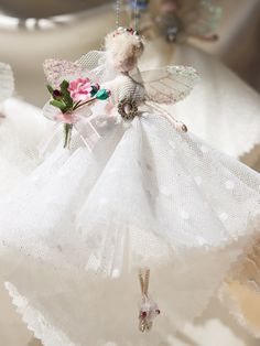 a white angel ornament hanging from a string with pink flowers and leaves on it