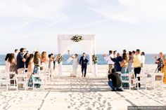 a couple getting married on the beach with their wedding party in front of them and an ocean view behind them