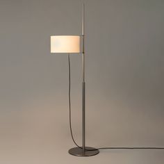 a floor lamp with a white shade on the base and a black cord plugged into it