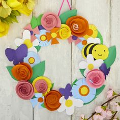 a paper flower wreath hanging on a wall next to flowers and a vase with yellow daisies