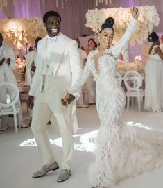 a man and woman dressed in white dancing at a wedding reception with chandeliers hanging from the ceiling