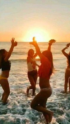 a group of people standing on top of a beach next to the ocean at sunset