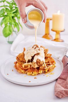 a person pouring syrup on top of a waffle covered in fried chicken and gravy